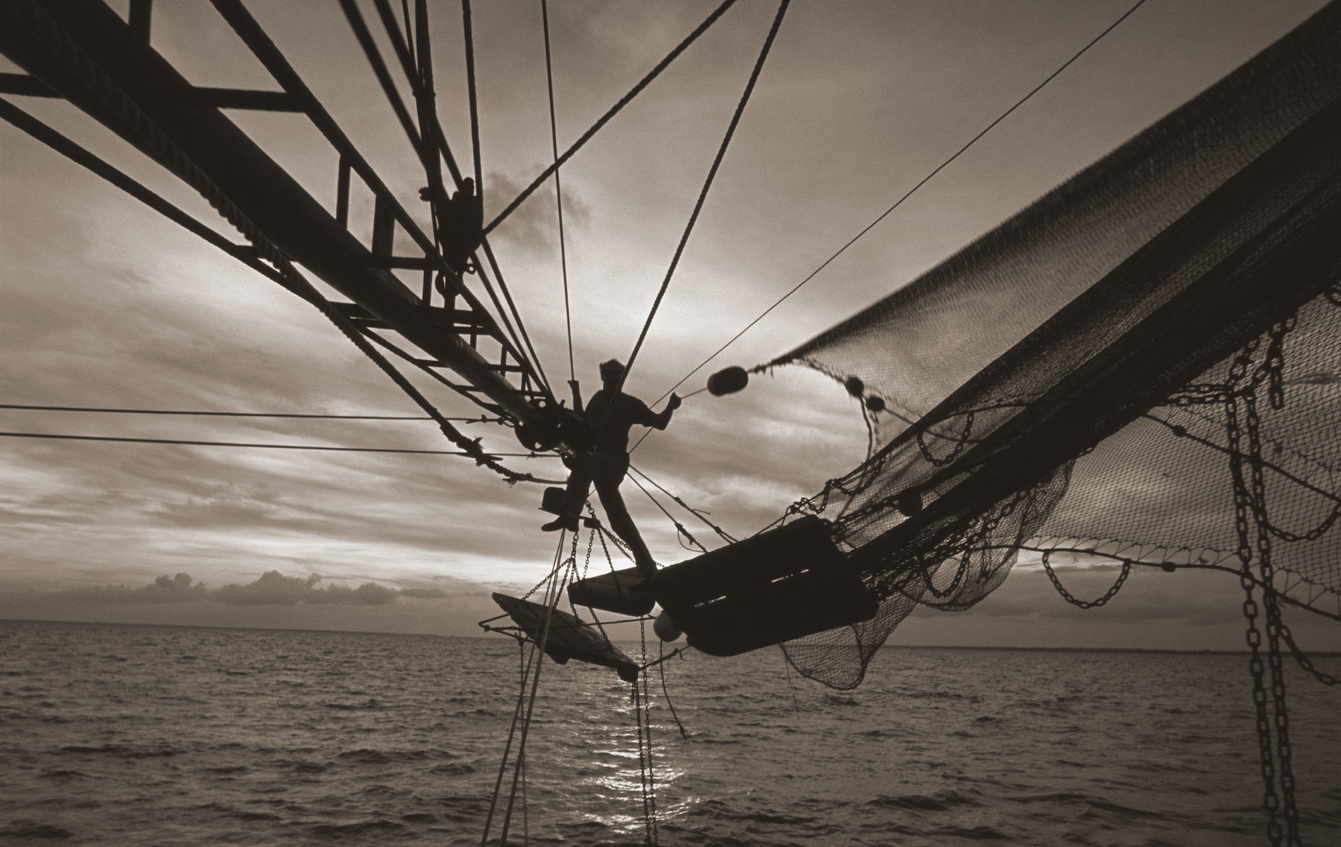 A Fisherman Casting A Net Over An Ocean Of Water Taken By Richard Bickel