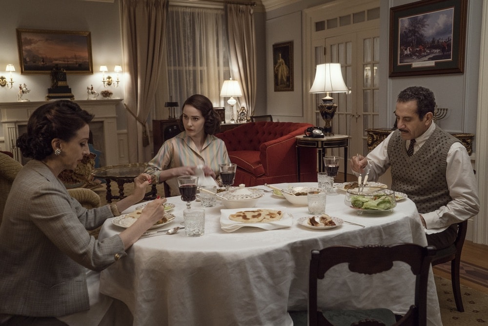 Marin Hinkle, Rachel Brosnahan and Tony Shalhoub in Season 1 of The Marvelous Mrs. Maisel eating dinner at the table in their apartment.