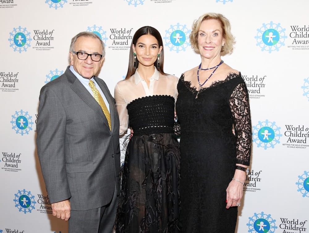 Harry Leibowitz, Lily Aldridge Followill, and Kay Isaacson-Leibowitz pose for a picture in front of the step and repeat banner. The step and repeat banner has a white background with the World of Children Award logo repeated.