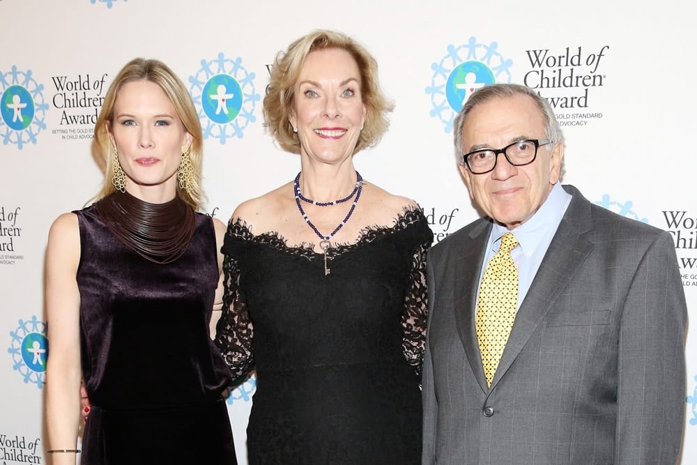 Stephanie March, Kay Isaacson-Leibowitz, and Harry Leibowitz pose for a picture in front of the step and repeat banner. The step and repeat banner has a white background with the World of Children Award logo repeated.