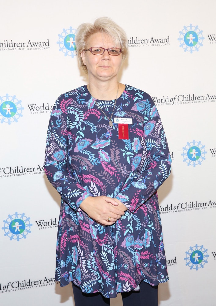 Honoree Dusica Popadic pose for a picture in front of the step and repeat banner. The step and repeat banner has a white background with the World of Children Award logo repeated.