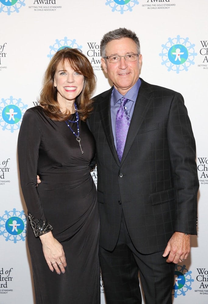 Lynn Naylor and Bill Naylor pose for a picture in front of the step and repeat banner. The step and repeat banner has a white background with the World of Children Award logo repeated.