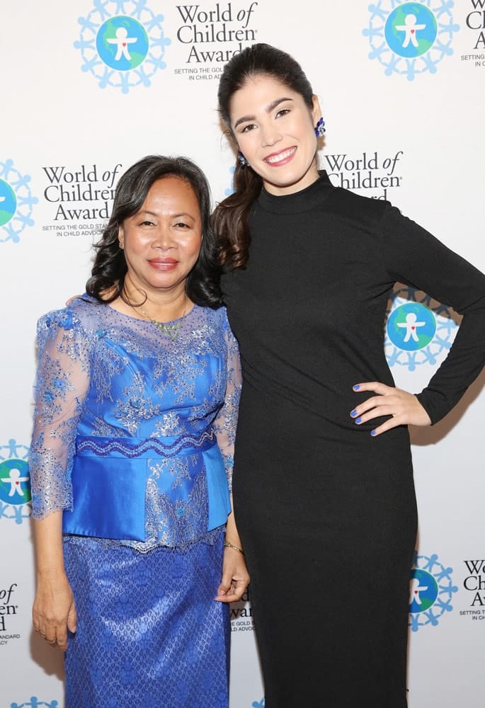 Ponheary Ly and Hannah Najar pose for a picture in front of the step and repeat banner. The step and repeat banner has a white background with the World of Children Award logo repeated.
