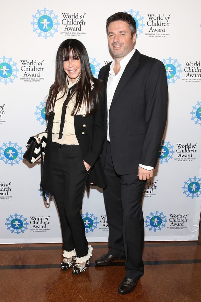 Sandy Sholl and Lionel Mendoza pose for a picture in front of the step and repeat banner. The step and repeat banner has a white background with the World of Children Award logo repeated.