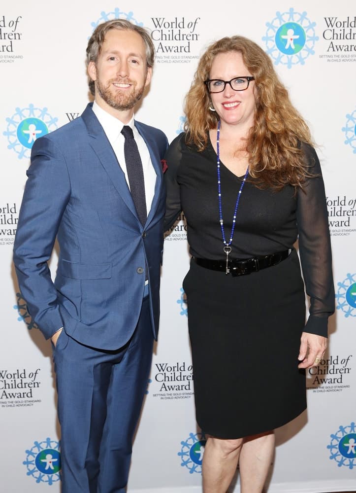 Adam Shulman and Heidi Nasher Fink pose for a picture in front of the step and repeat banner. The step and repeat banner has a white background with the World of Children Award logo repeated.
