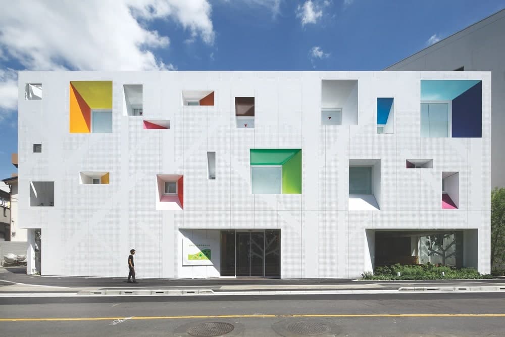 Sugamo Shinkin Bank’s Tokiwadai Branch facade with silhouettes of trees and fourteen colors within the windows arranged in a rhythmical pattern