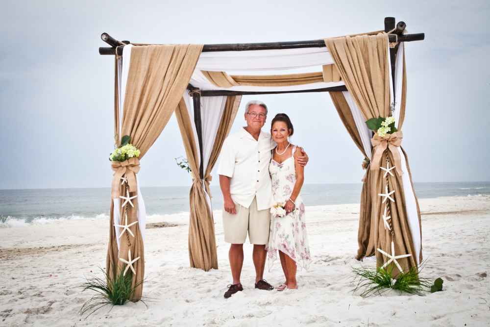 Husband and wife stand under beach alter