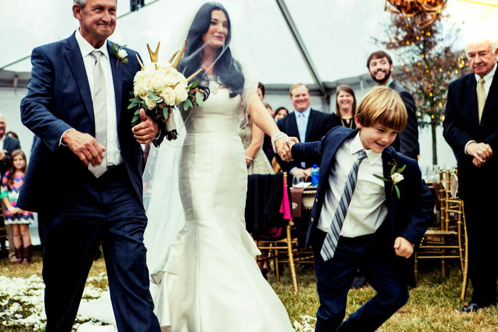 Little boy holds bride's hand with father down aisle