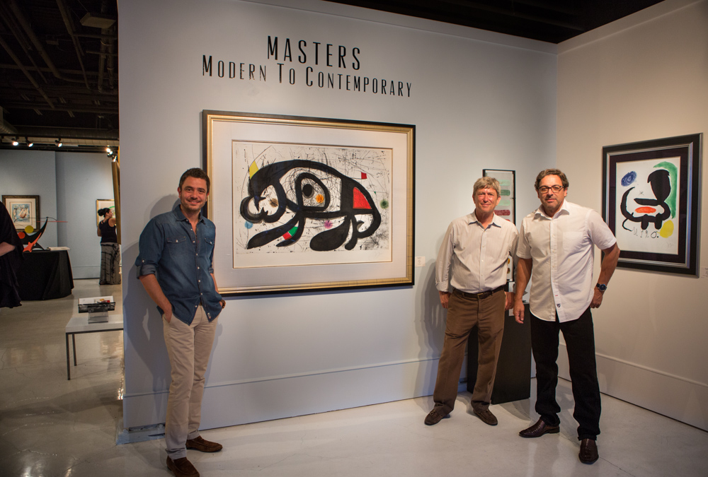 Three men posing with paintings in art gallery