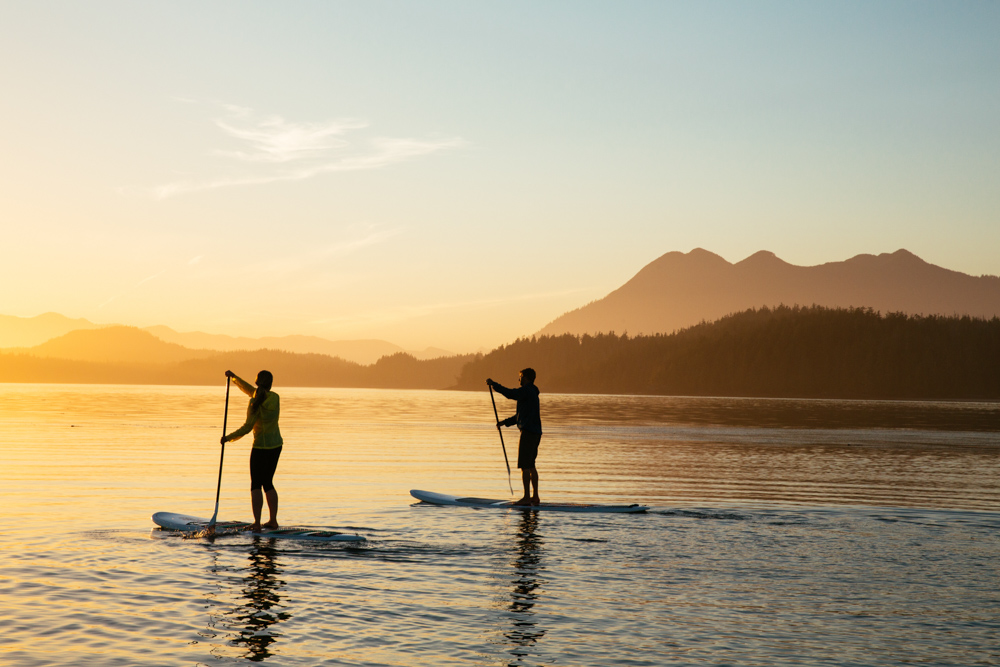 Two people paddleboarding on the water with mountains sitting in the background in Vancouver Island, Canada