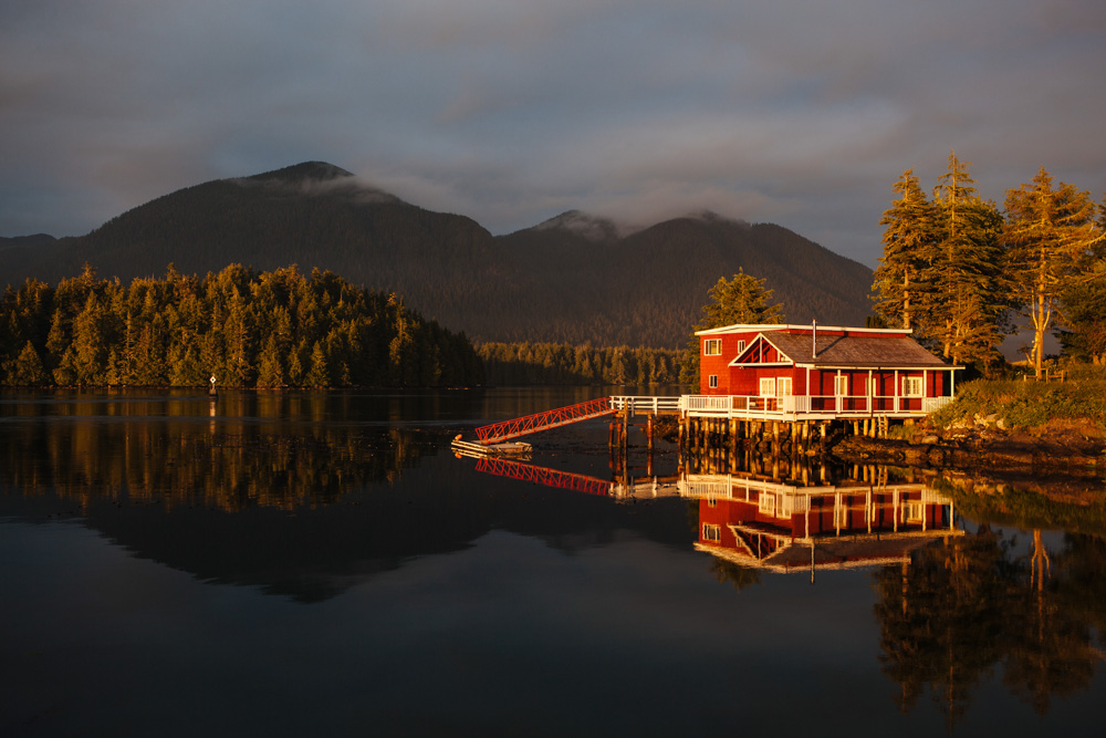 Red lake house sitting on edge of water with mountains in the distance in Vancouver Island, Canada