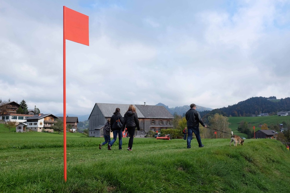 Visitors walk path of orange flags through pastures Werkraum Bregenzerwald Austria