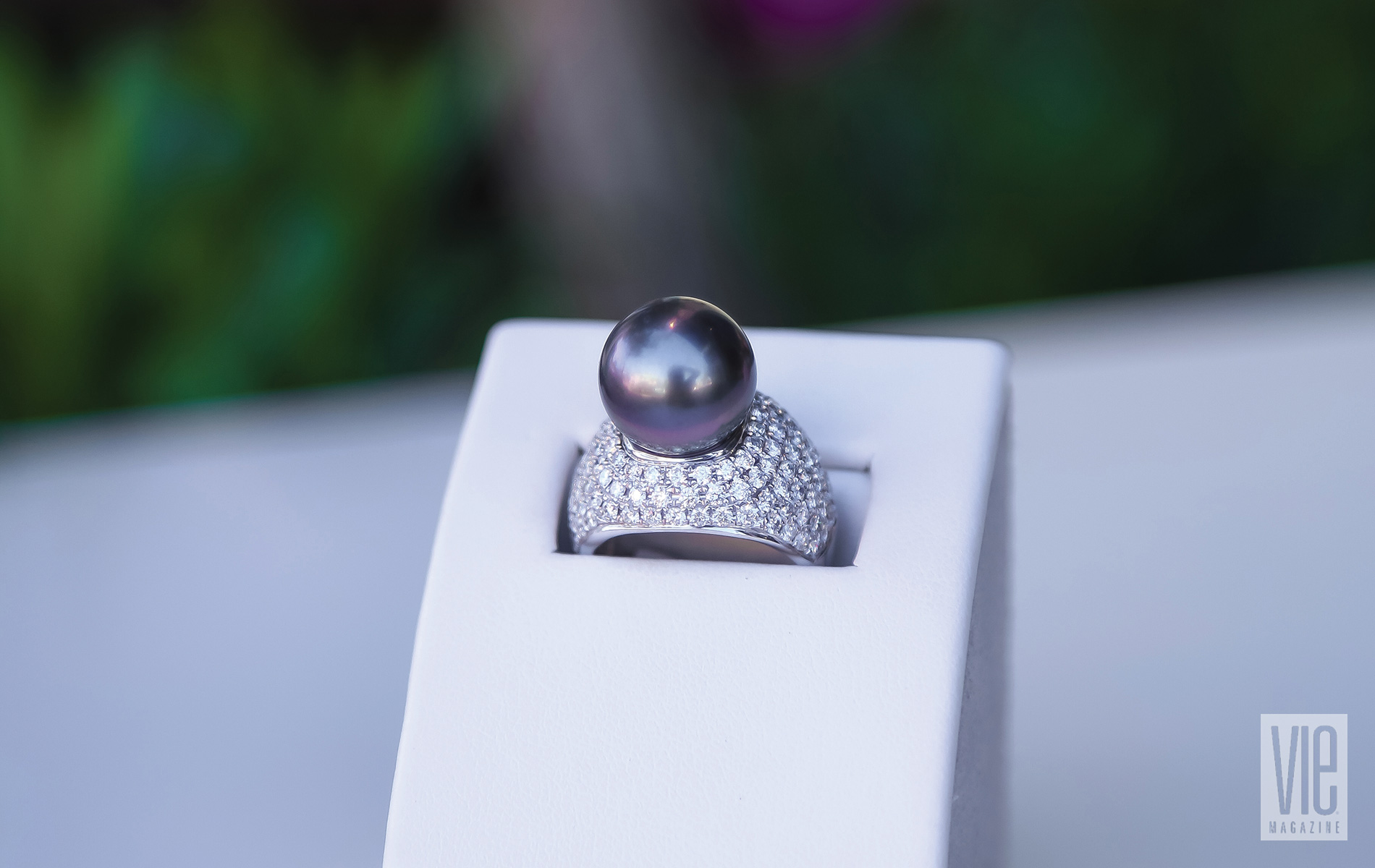 A Big Black Pearl Cocktail Ring Surrounded By A Setting Of Pave Diamonds Resting On A Ring Case