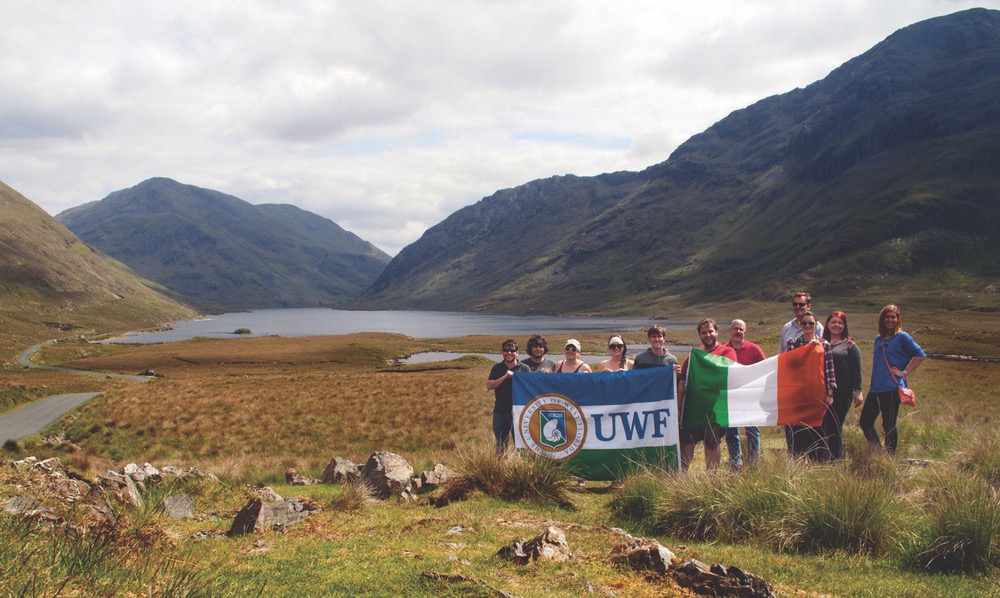 University of West Florida Irish Experience Program Standing With UWF And Irish Flag With A Backdrop of Mountains