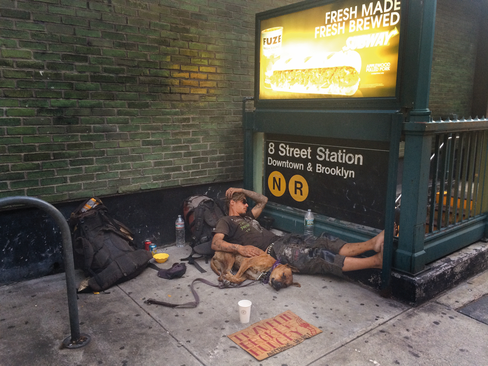 Homeless man and pet sleeping outside subway station