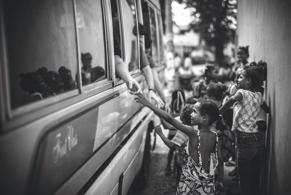 Black and white photo of San Cristóbal, Dominican Republic orphan at orphanage reaching out to passenger on bus. Chandler Williams, Modus Photography.
