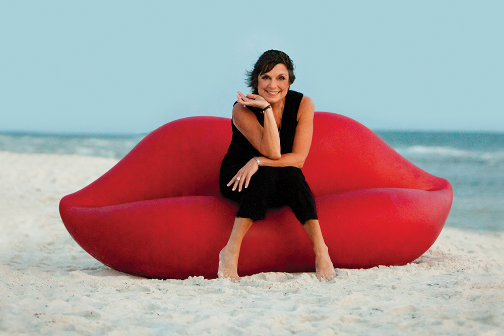 Linda Miller in her signature red lips sofa on the beach luxury real estate