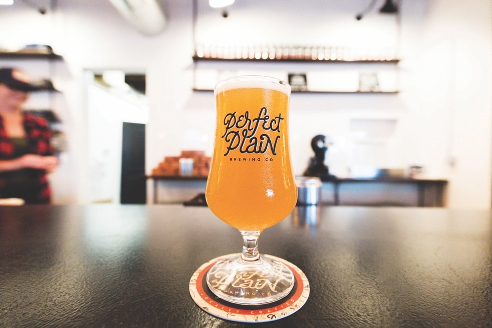 Shot of a beer from Perfect Plain Brewing Company, located in downtown Pensacola, Florida. The clear glass has their logo in black and is sitting on a black counter top at the bar