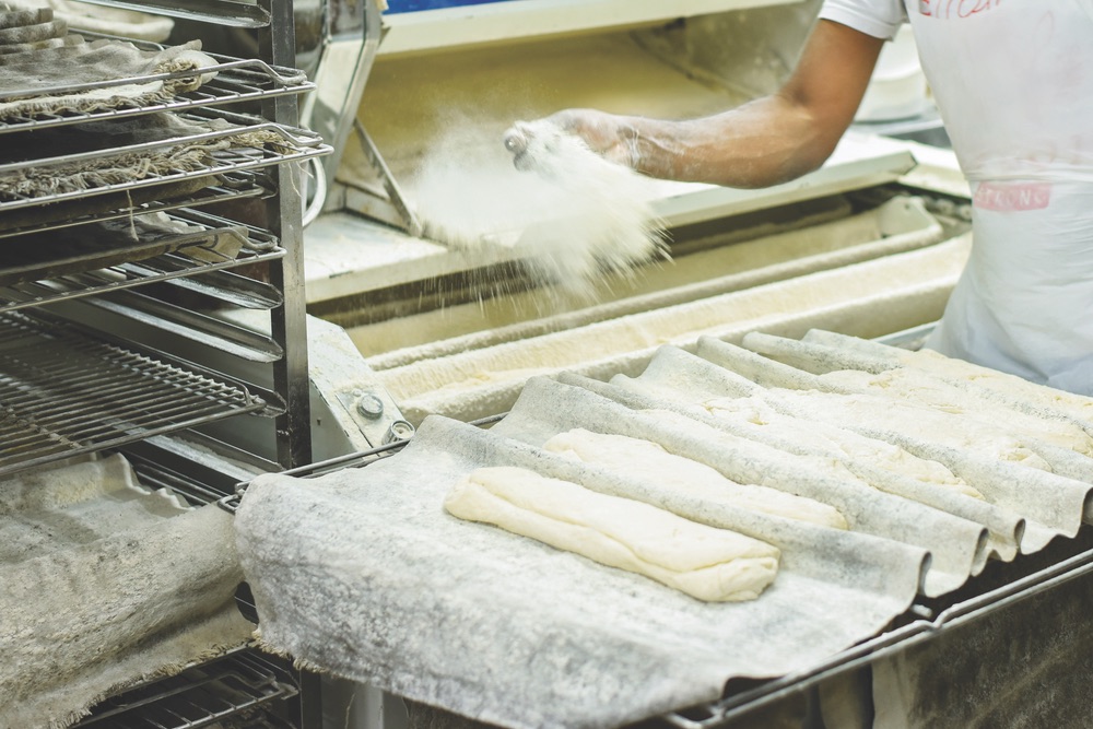 A baker at authentic boulangerie Grégory Desfoux sprinkles flour onto baguette dough during a behind-the-scenes tour. Photo by Benoit Fortrye, courtesy of Paris a Dream