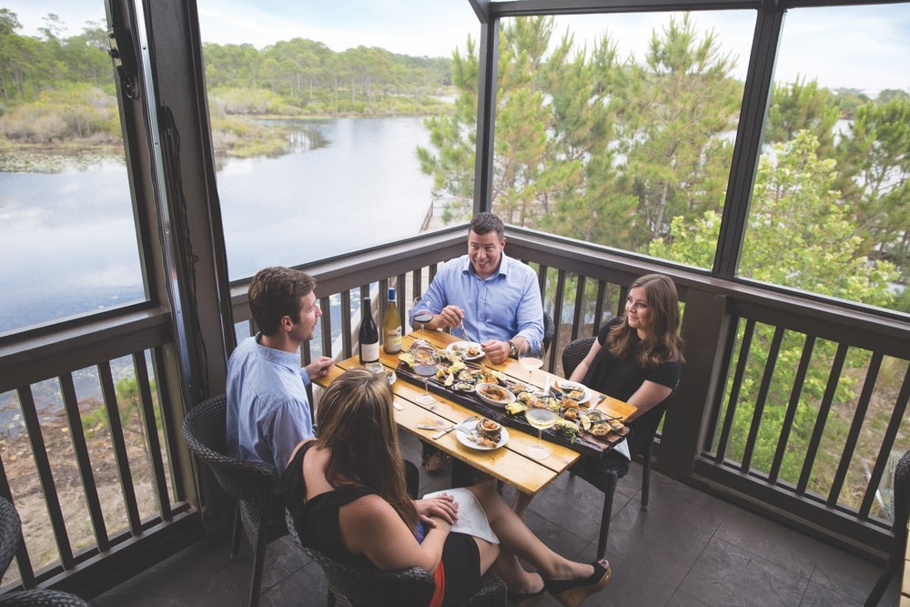 Two couples on a double date drinking wine and eating dinner in a screened in porch in a restaurant that's right on the lake in Walton County, Florida