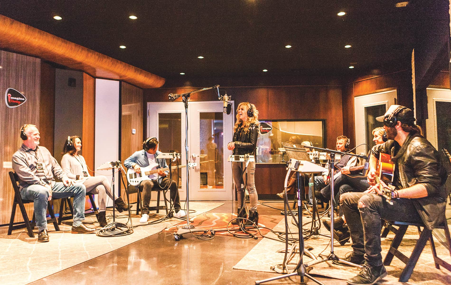 Recording artist Natalie Stovall sings a new song during a live Imagine Recordings session with studio musicians while attendees listen through headphones.