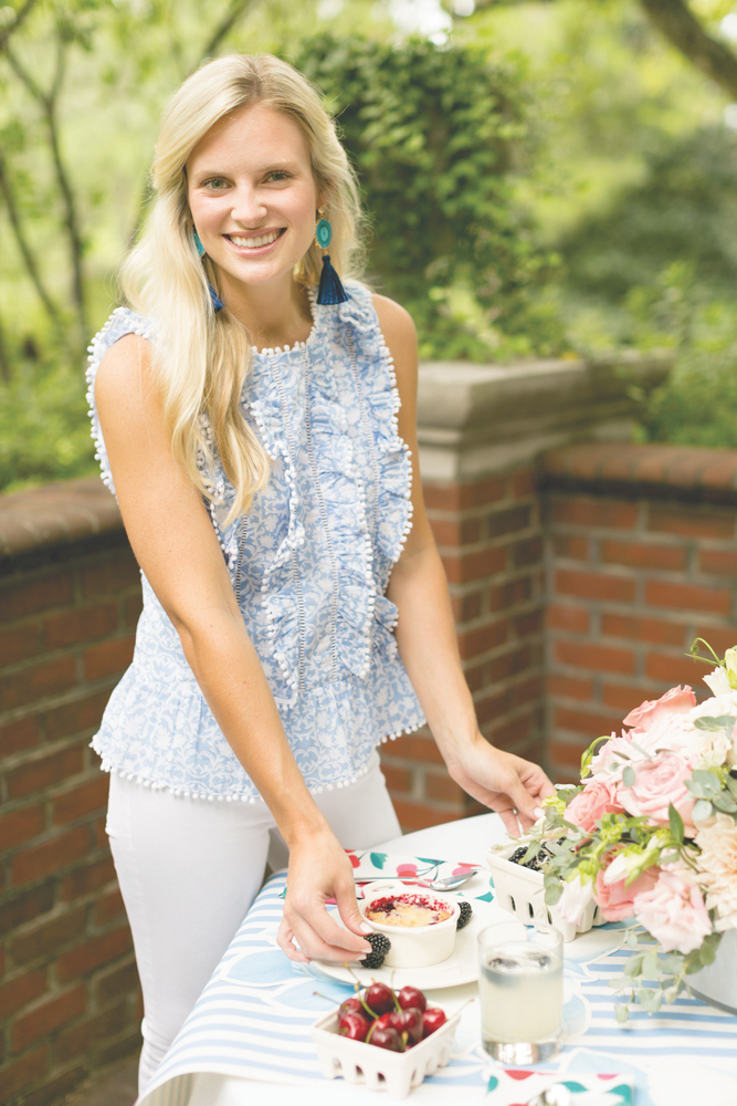 Elisabeth Farris outside on a back patio serving her blackberry cobbler dessert to a table with fresh flowers and fruit