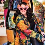 Ashley Longshore wearing a Gucci coat sitting in a customized Longshore chair on the seventh floor of Bergdorf Goodman during her pop-up gallery installment