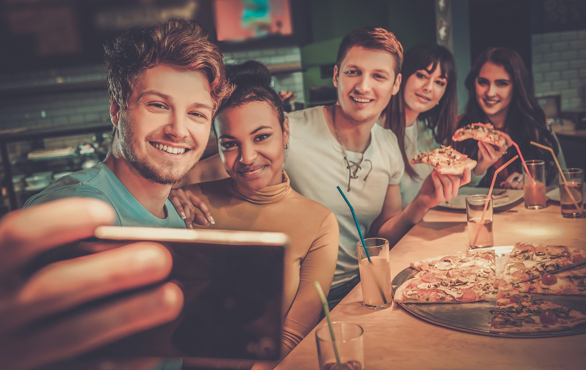 Cheerful group of five friends having fun eating pizza and taking a selfie.