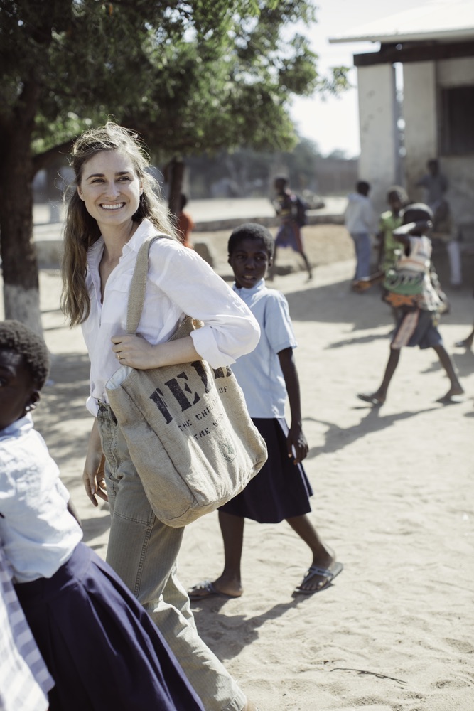 Lauren with the FEED 1 tote bag and small children walking in a dirt yard