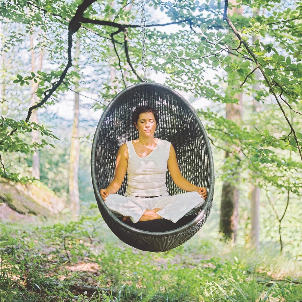 A woman meditating in a hanging seat in the forest at La Clairière in Alsace, France