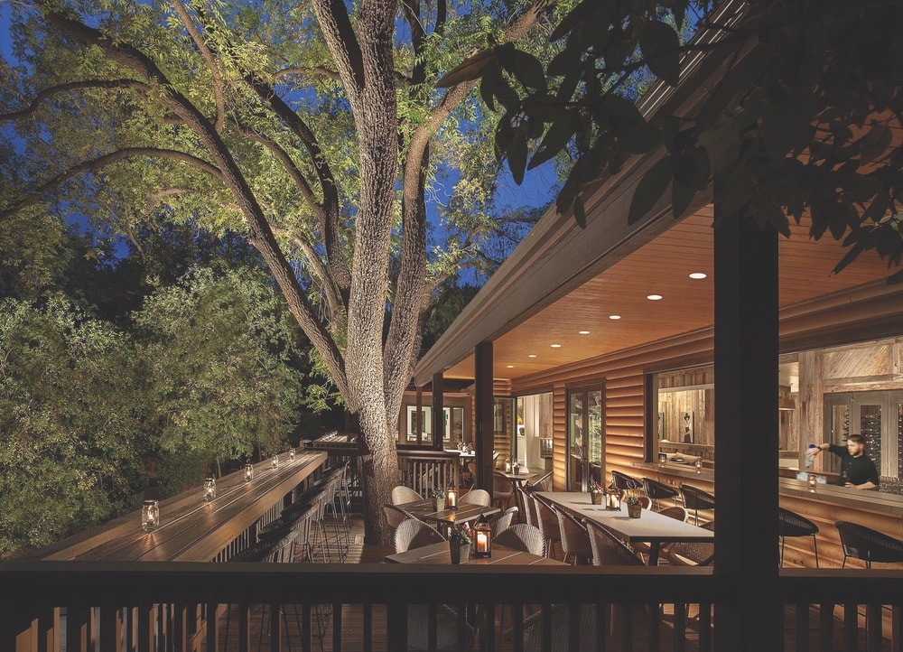 A view of the terrace at night through the trees at L’Auberge’s Etch Kitchen & Bar, situated beneath towering sycamore trees.