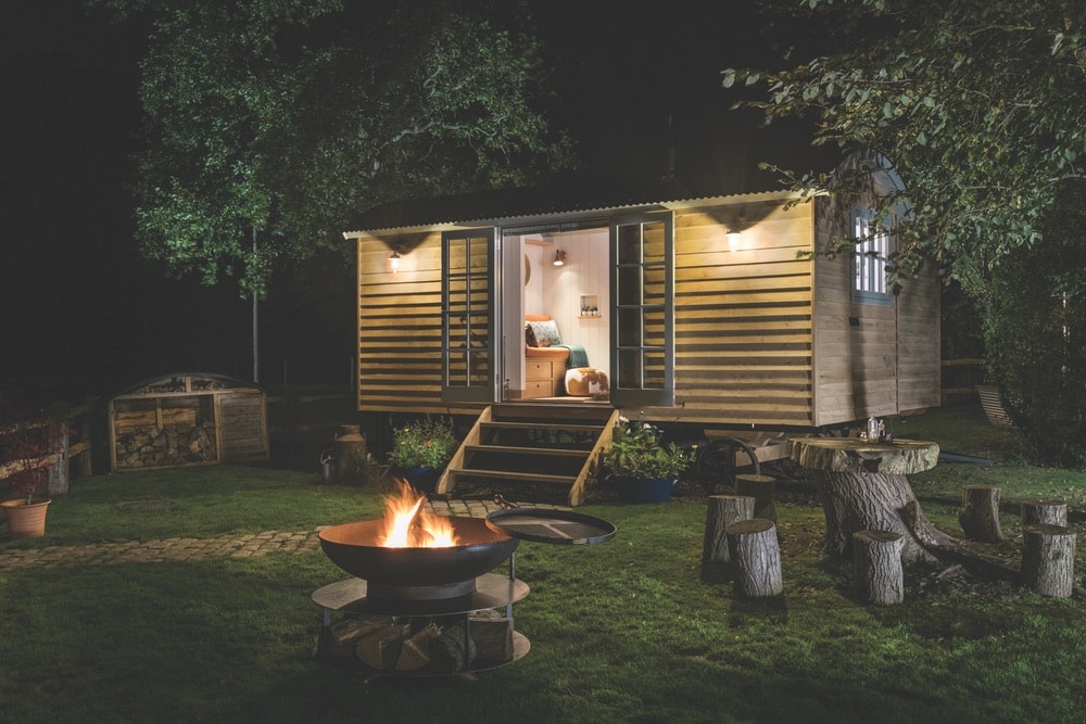 Quaint, hideaway cabin at the Fish Hotel in the Cotswolds, England with a campfire and fresh wood at night