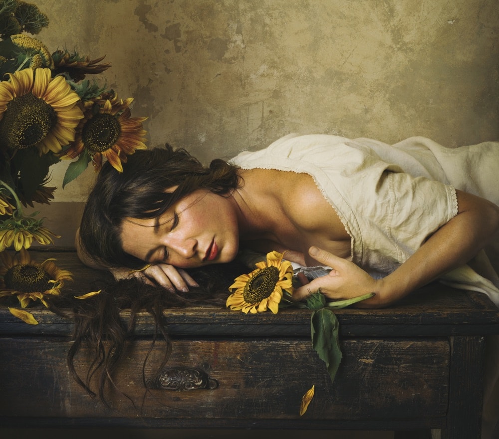 Photograph by Jamie Beck showing a female leaned over a table holding a sunflower