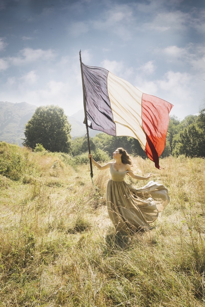 Photograph by Jamie Beck showing a female in a field holding a large French flag