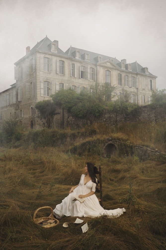 Photograph by Jamie Beck showing a female sitting in a chair in front of a large French house