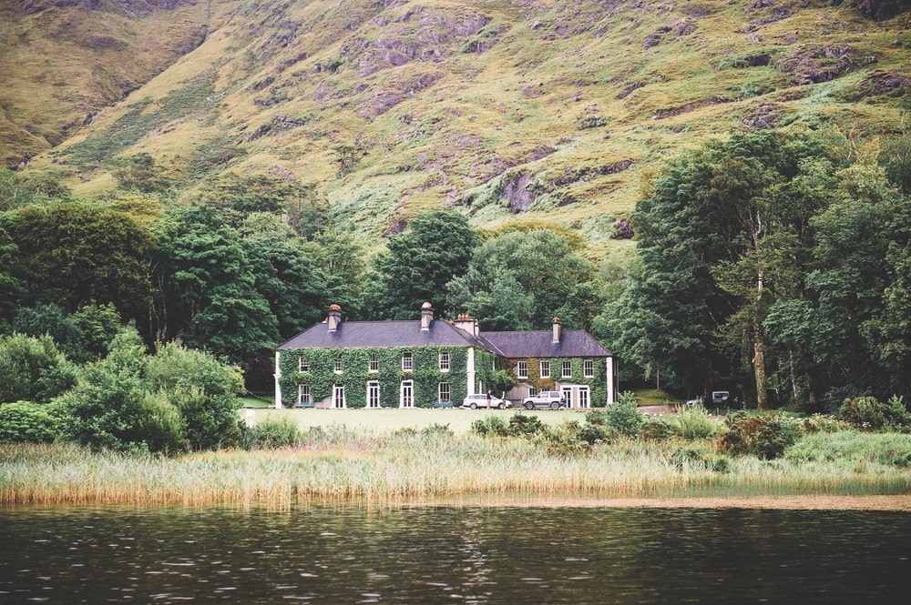 Beautiful ivy two-story home sitting on the edge of the water at the foothills of a mountain in Ireland
