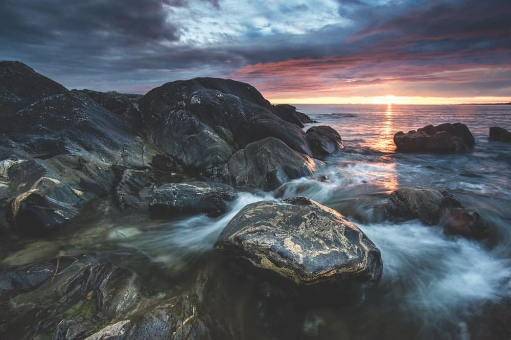 View of the Errislannan shoreline, dark rocks, and stormy clouds at sunset in Ireland