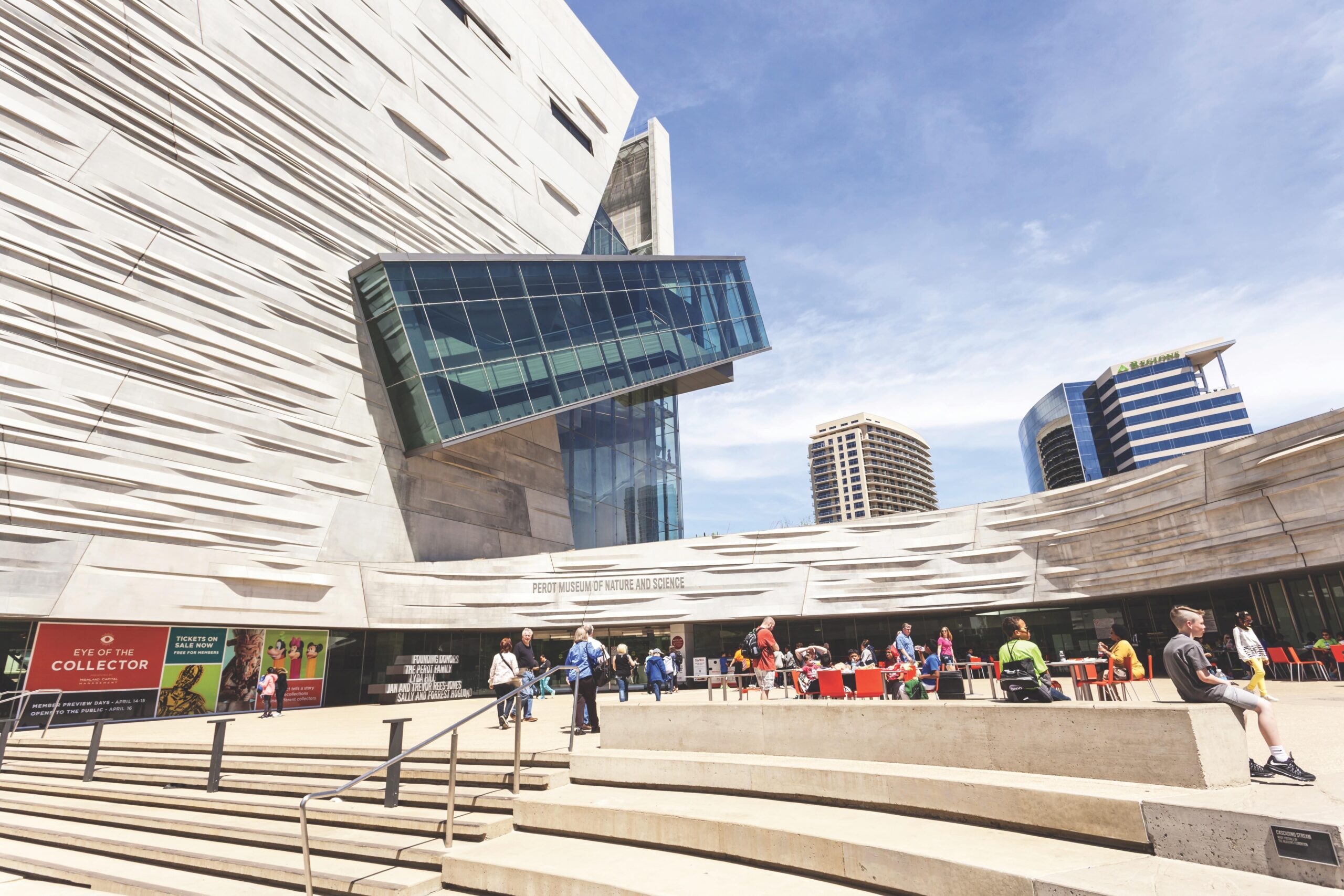 The Perot Museum of Nature and Science in Dallas has a modern exterior with people enjoying a beautiful sunny day.