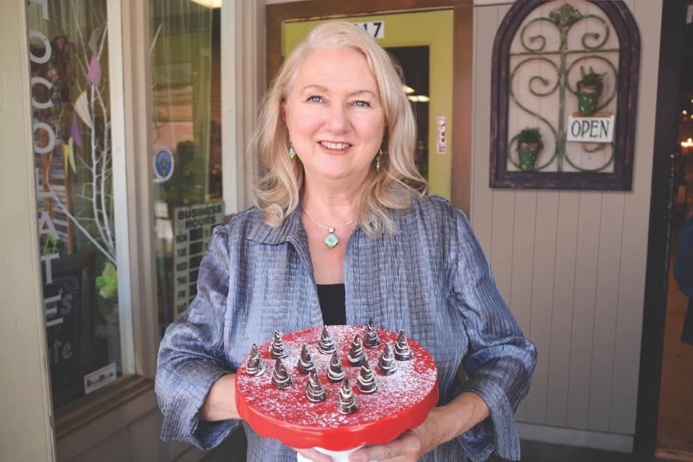 Dr. Sue Williams holding a red tray of Christmas chocolates in front of her store in Dallas, Texas