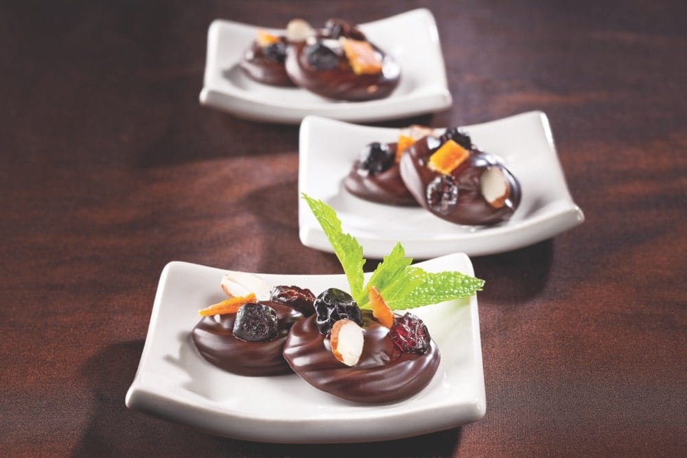Three pairs of mendiants, which is French chocolate disks studded with nuts and dried fruits, on small, white plates