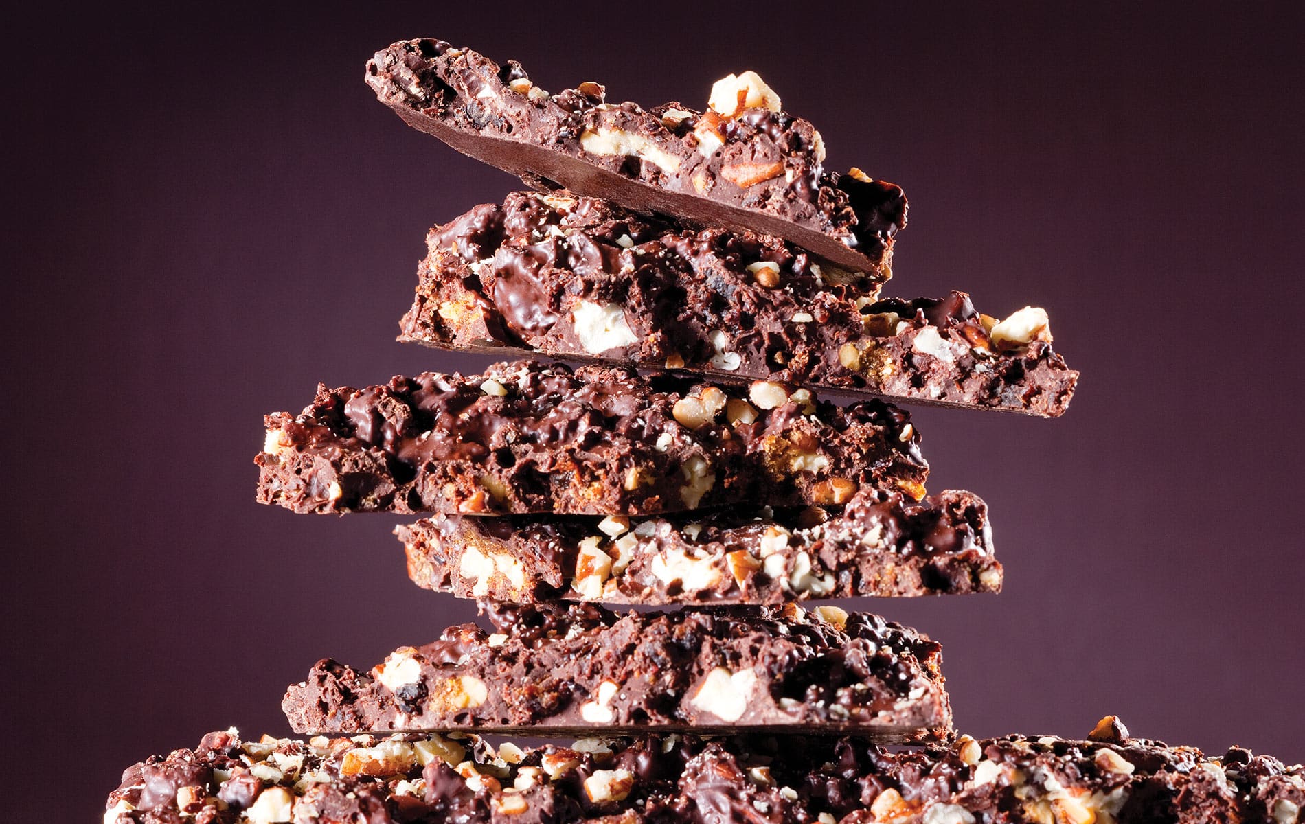 Six pieces of Dr. Sue's delicious hazelnut bark stacked on top of each other in front of a deep purple background