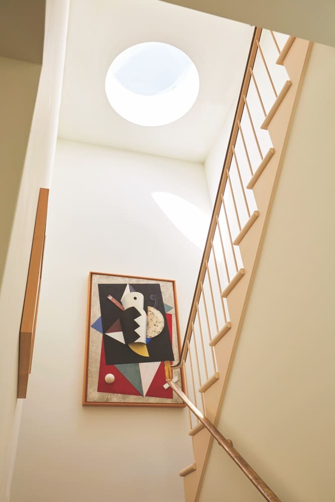 Art on the wall in the stairwell with a natural light pouring through the skylight at Paula Lambert's Turtle Creek home in Dallas, Texas