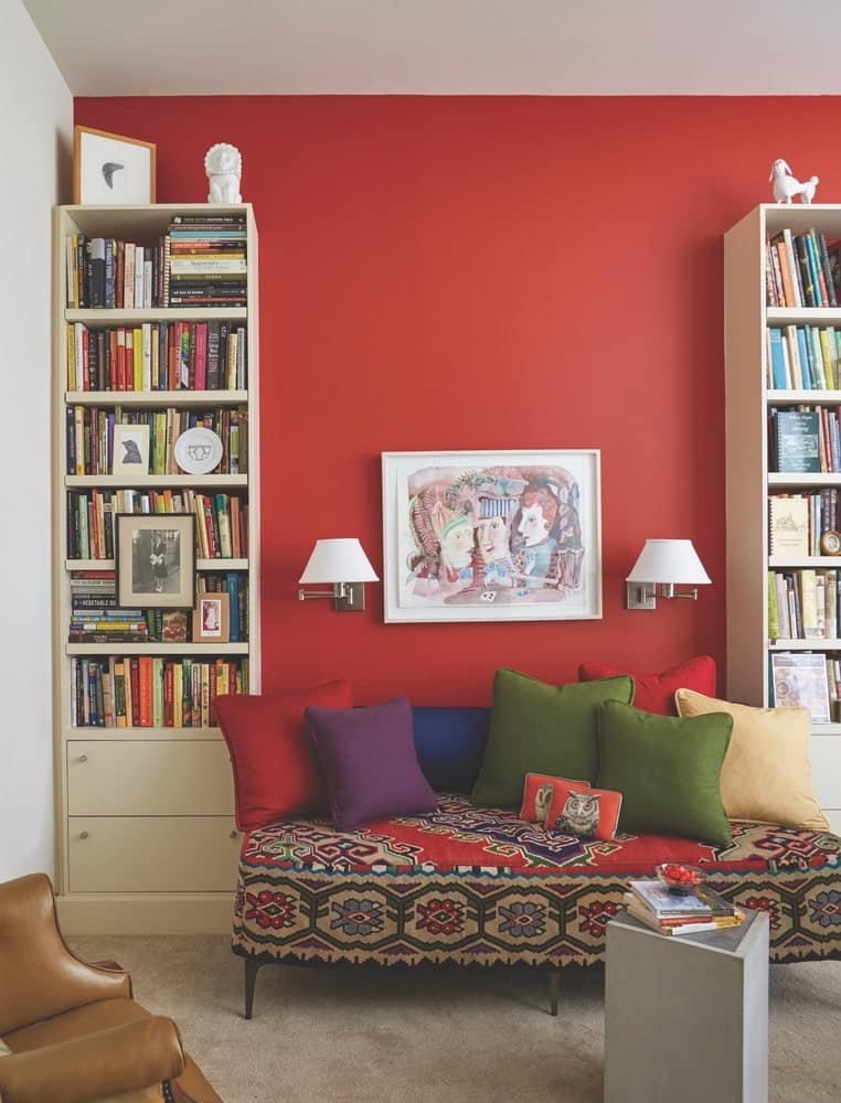 A sitting area in Paula Lambert's home office with red walls, bookshelves full of books, and a fun-patterned lounge couch at her Turtle Creek home in Dallas, Texas