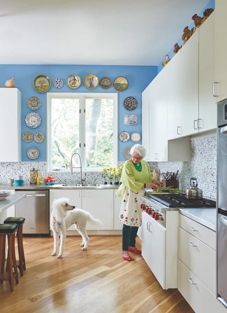 Paula Lambert in her blue and white kitchen prepping food with her white dog at her Turtle Creek home in Dallas, Texas