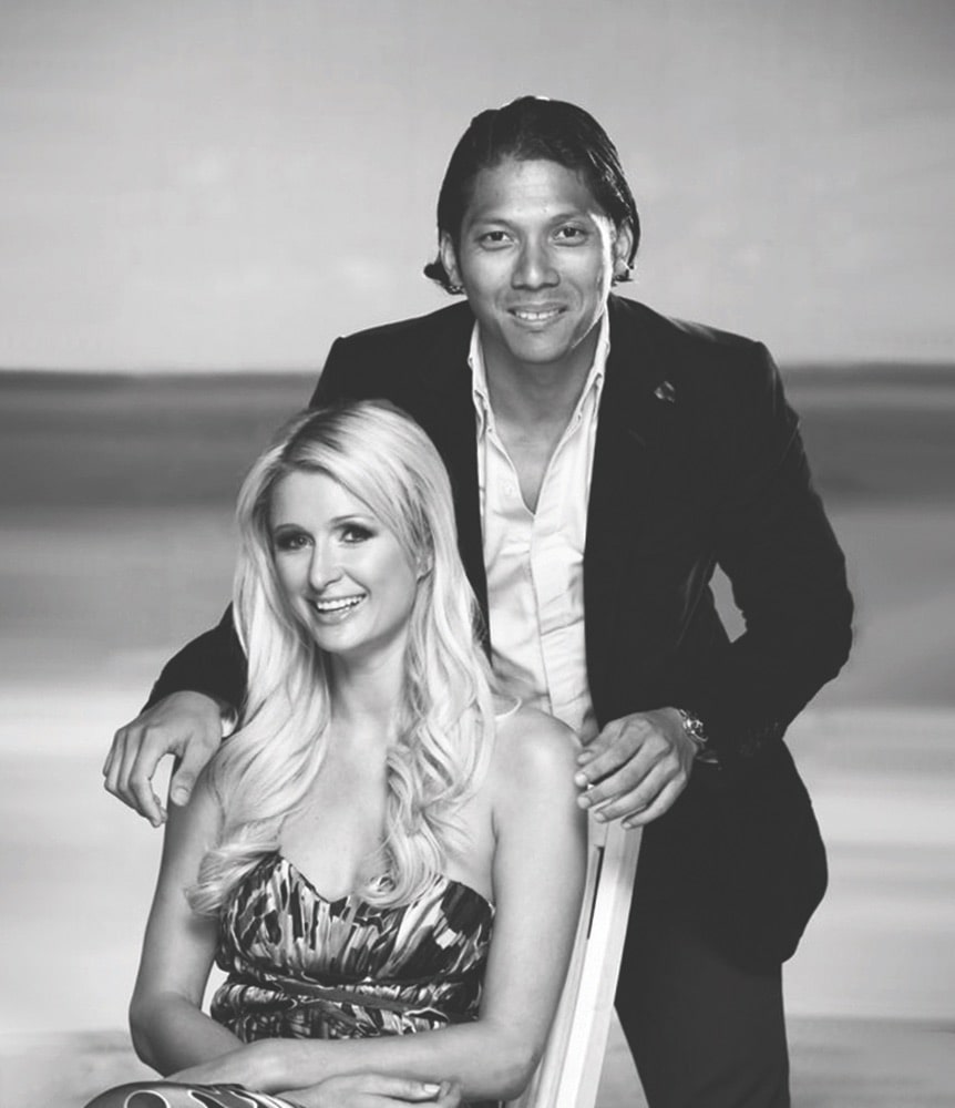 Black and white image of Robbie Antonio posing behind Paris Hilton, who is sitting down