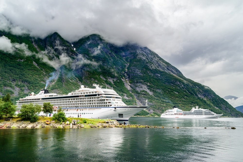 Travel documentary of the luxury cruise ships Viking Star and Seaborn Quest moored in fjord. High and steep mountainside in background with rainclouds in the sky.