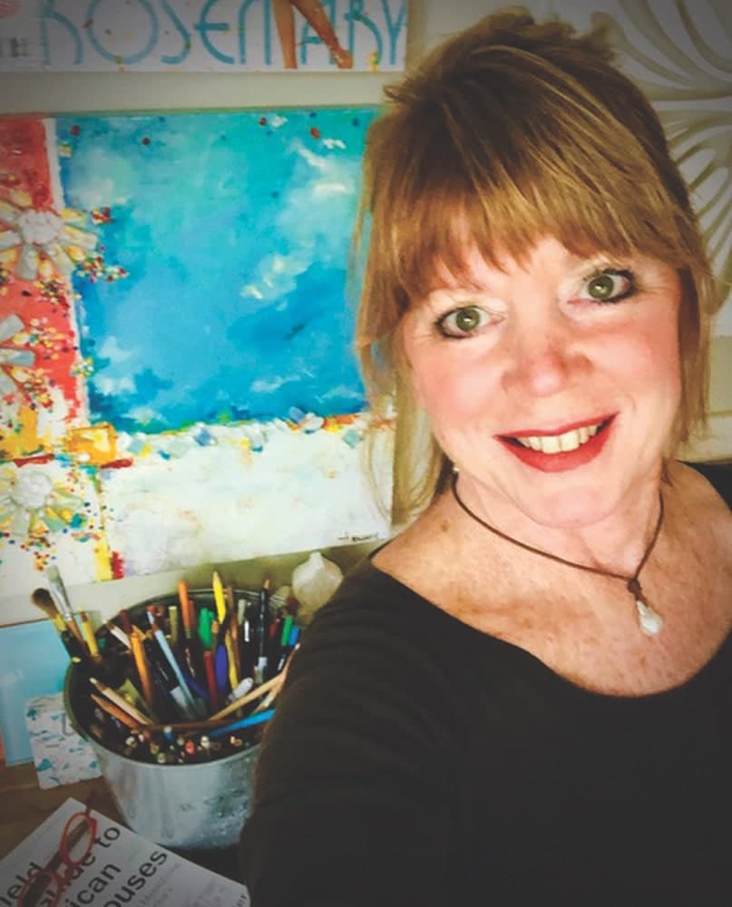 Artist Tamera “Tammy” Massey taking a selfie in front of her artwork and art supplies