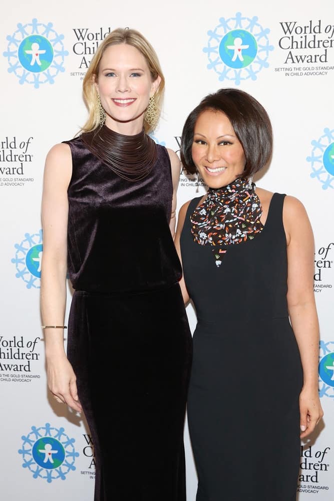 Stephanie March and Alina Cho pose for a picture in front of the step and repeat banner. The step and repeat banner has a white background with the World of Children Award logo repeated.