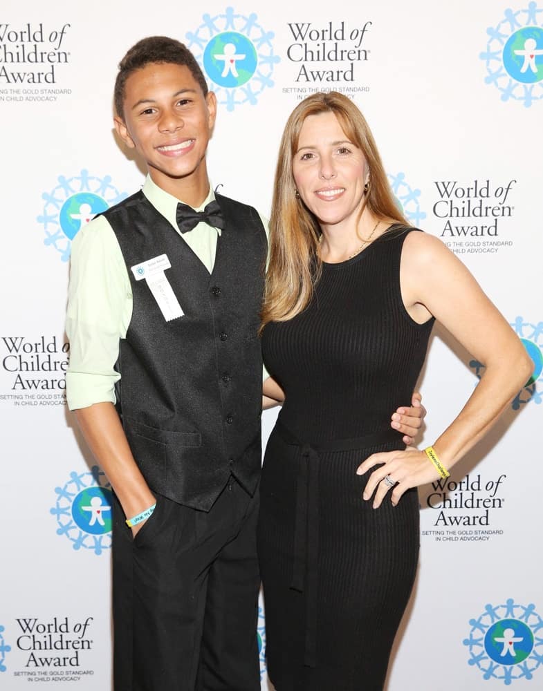 Jaylen Arnold and Robin Arnold pose for a picture in front of the step and repeat banner. The step and repeat banner has a white background with the World of Children Award logo repeated.