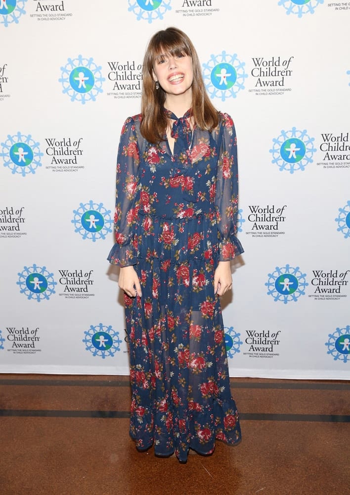 Claire Wineland pose for a picture in front of the step and repeat banner. The step and repeat banner has a white background with the World of Children Award logo repeated.